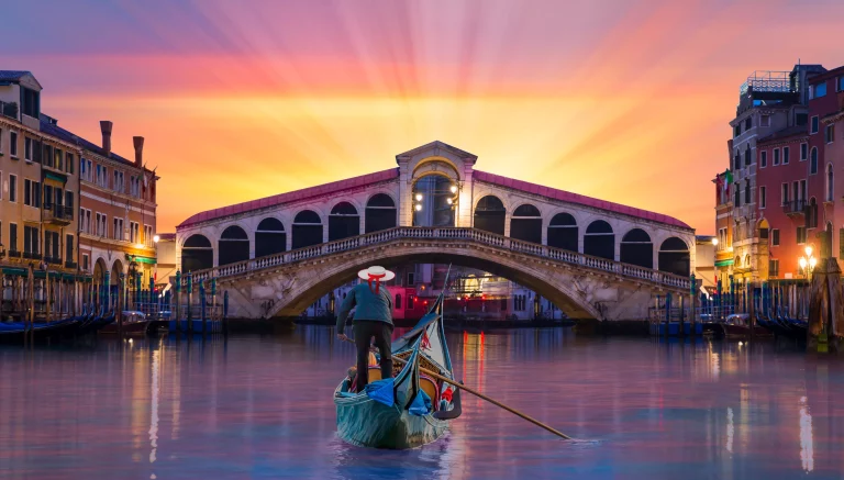 Gondolier carries tourists on gondola near Rialto Bridge - Venice, Italy