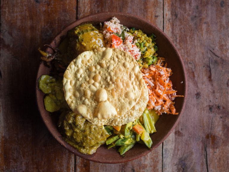 Bowl of variety of traditional vegan Sri Lankan food with different curries, papadum, rice, sambol, dal and vegetables,