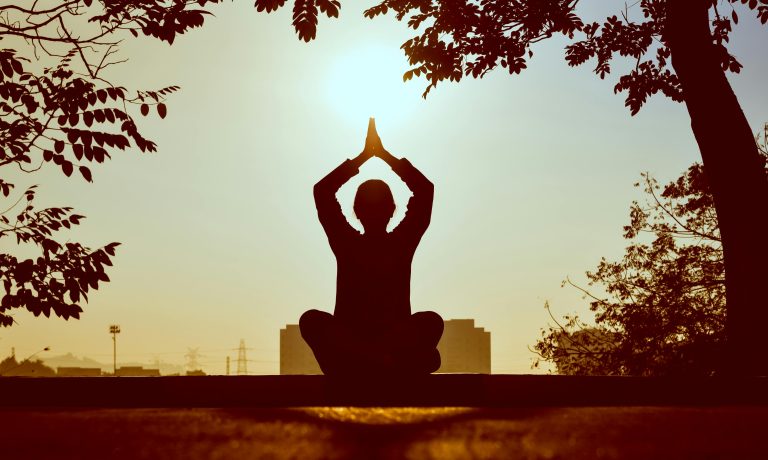 Silhouette of a person practicing yoga outdoors during sunrise, creating a calming atmosphere