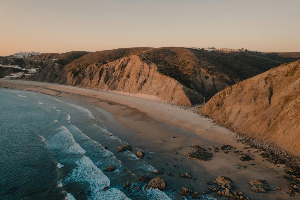 Drone view of Aljezur's rugged coastline in Faro, Portugal with waves crashing at sunset.