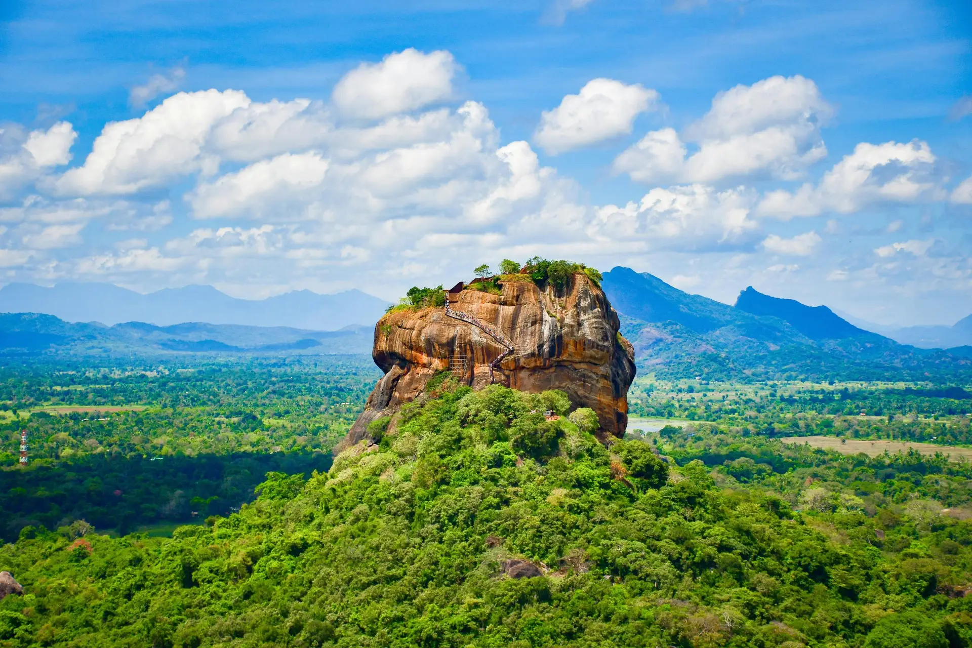 Explore the iconic Sigiriya Lion Rock surrounded by lush greenery and vibrant blue skies in Sri Lanka.