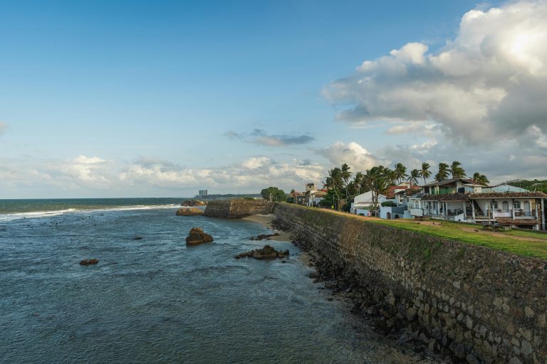 Picturesque seaside view of the historic Galle Fort in Sri Lanka, featuring the coastal wall and ocean under a cloudy sky.