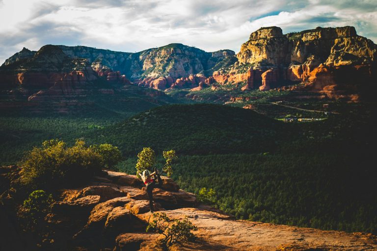 Woman performing yoga pose on a rocky ledge against the stunning Sedona landscape during sunset