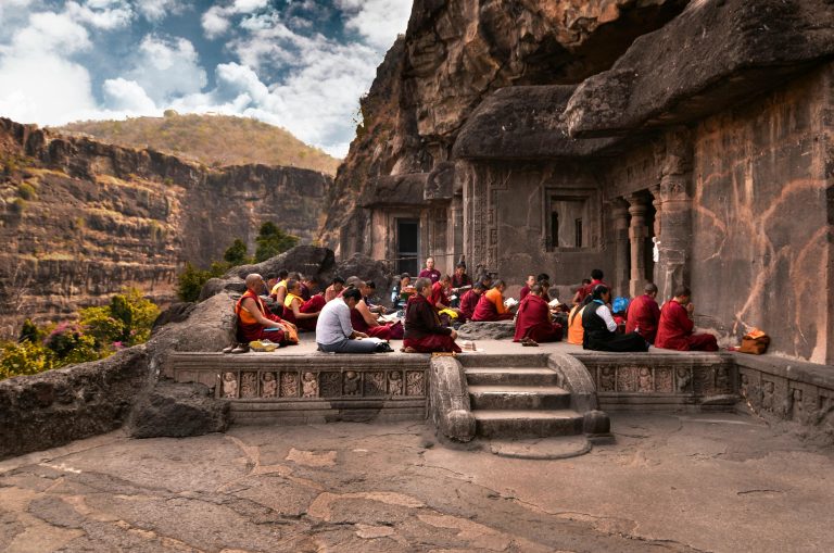 Group of monks in traditional robes meditating at an ancient rock temple during the day