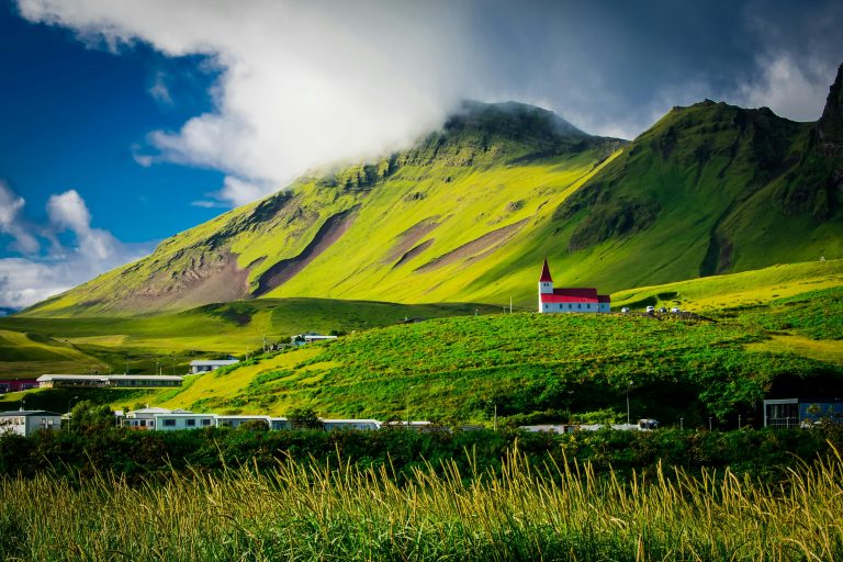 Beautiful landscape of a red-roofed church nestled in lush green hills under a vibrant sky in Iceland